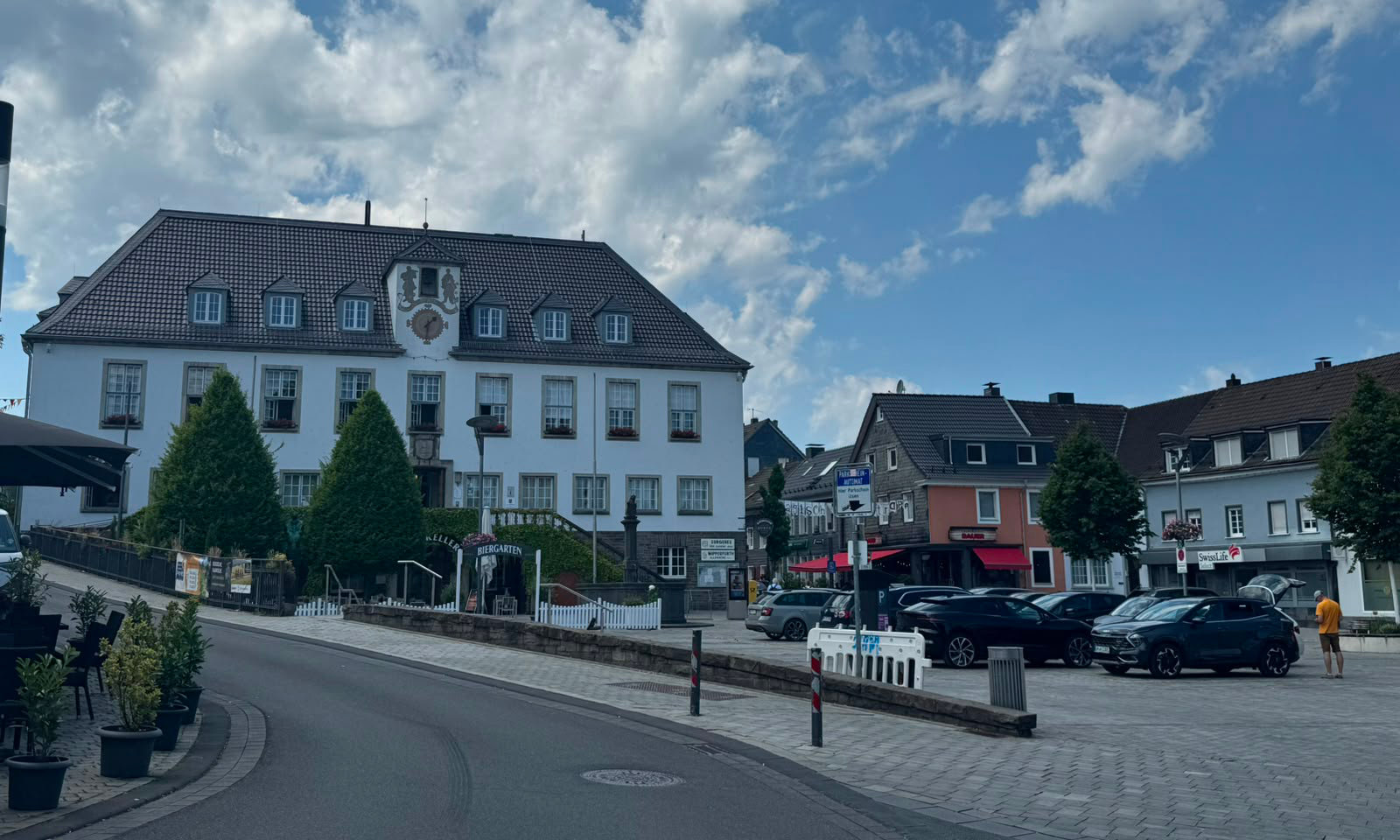 Der Marktplatz von Wipperfürth an einem Sommertag: das historische Rathaus mit Turmuhr und Ratskeller-Biergarten, daneben Geschäfte und Bäume