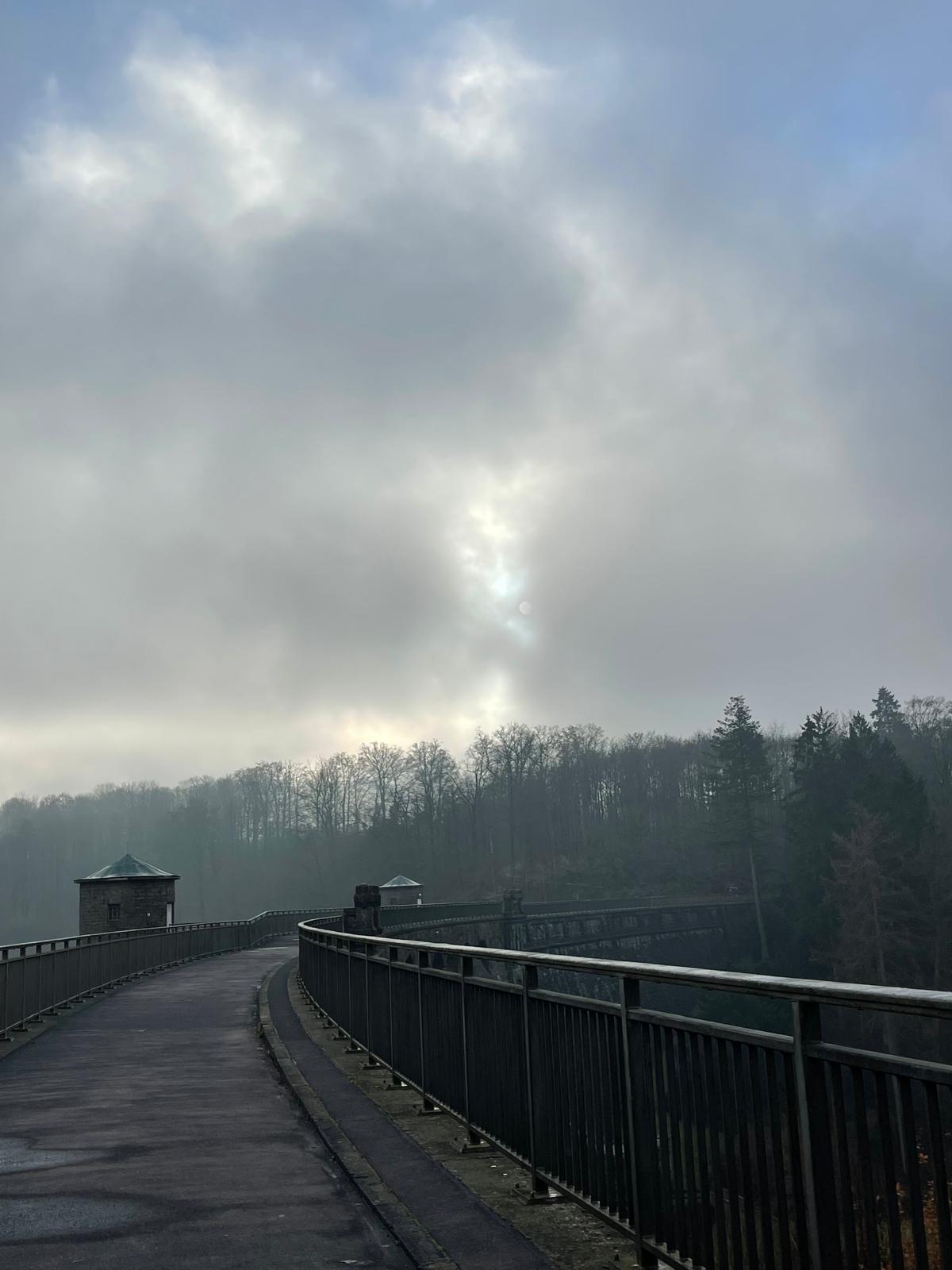 Fußweg über die Staumauer einer Talsperre mit zwei Natursteintürmen im Nebel